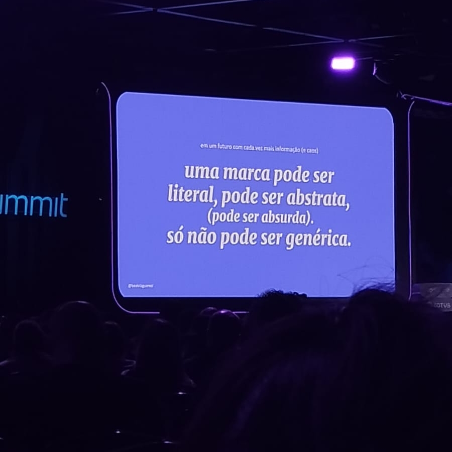 Slide apresentado no RD Summit pela Beatriz Guarezi com fundo roxo exibindo a frase: ‘uma marca pode ser literal, pode ser abstrata, pode ser absurda, só não pode ser genérica’. A imagem mostra o público assistindo à palestra sobre branding e diferenciação de marca.