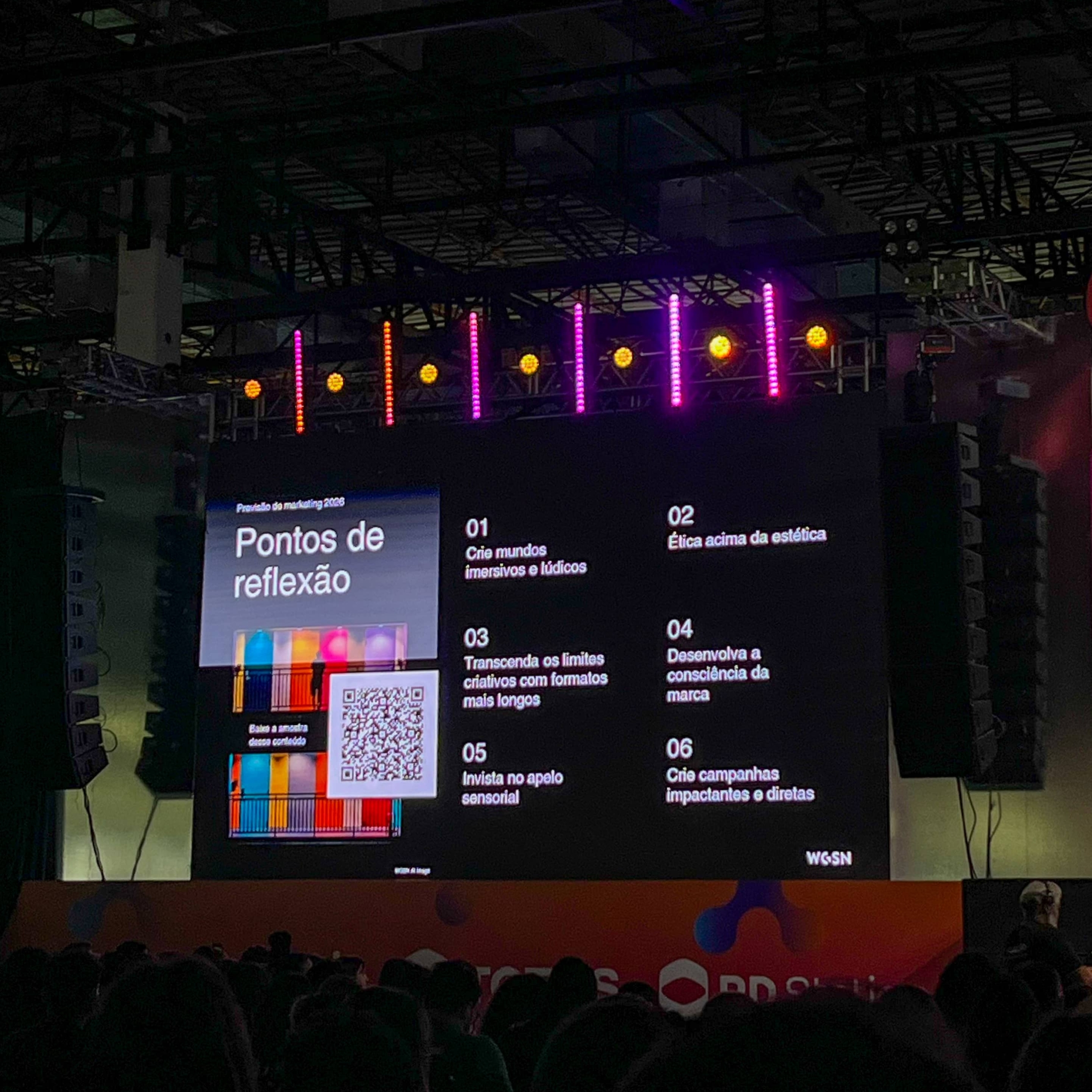 Slide exibido no RD Summit com o título 'Pontos de reflexão', apresentando seis diretrizes de marketing para 2026: criar mundos imersivos e lúdicos, priorizar ética sobre estética, transcender limites criativos com formatos mais longos, desenvolver a consciência da marca, investir no apelo sensorial e criar campanhas impactantes e diretas. A imagem mostra também um QR Code, elementos coloridos e o público assistindo ao conteúdo.